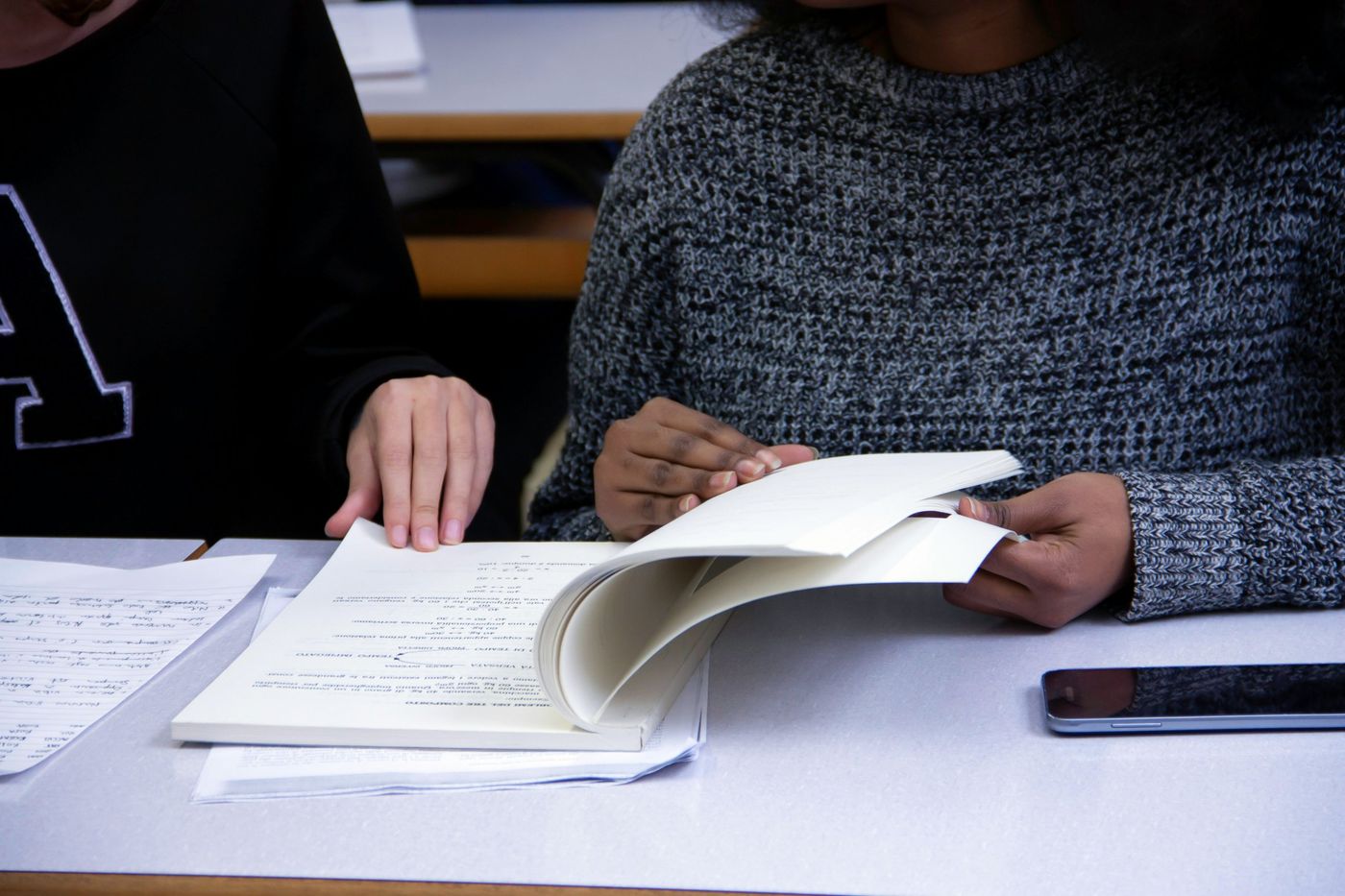 Two people studying side by side from one book, a phone lying face down on the table